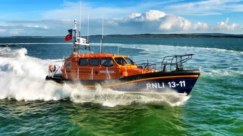 RNLI/Steve Lowe An orange and blue Shannon class RNLI lifeboat cutting through the waves on the sea during a call-out.