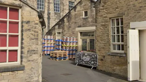 Google Metal barrels and a fence sign reading Amity outside some mill buildings.