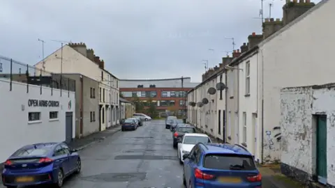 A screengrab of a Google Streetview image of Harford Street in Portadown. The street is lined by two and three-storey terraced houses and there is a plain grey building on the left with a sign that says "Open Arms Church". The street has no traffic exit at its far end. 