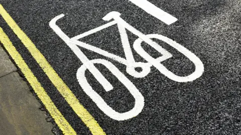 A cycle lane marked by a large emblem of a bicycle, with double yellow lines at the edge. 