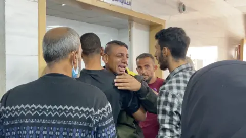 BBC An emotional man is comforted by other men at the Kamal Adwan Hospital 