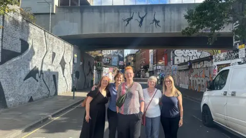 Een groep vrouwen voor Banksy's swingende aapschilderij in Shoreditch