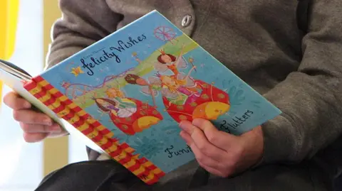 A picture of a child reading a book. It has a blue front and reads 'Felicity wishes'
