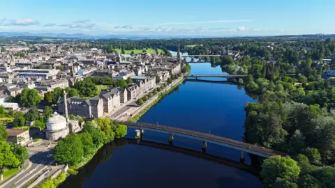 Kevin Hamill A birdseye view of Perth. The River Tay runs through the middle of the city and there are three bridges crossing it. Buildings and trees line either side of the river.