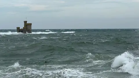 Choppy seas around the Tower of Refuge in Douglas Bay. The sea is dark and the sky is cloudy with a hint of blue.
