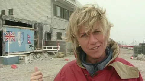 A younger Sally Taylor standing in front of a bombed-looking part of Bosnia.