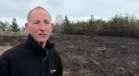 Howard Inns looking at the camera has blue eyes, grey hair and is wearing a black fleece.