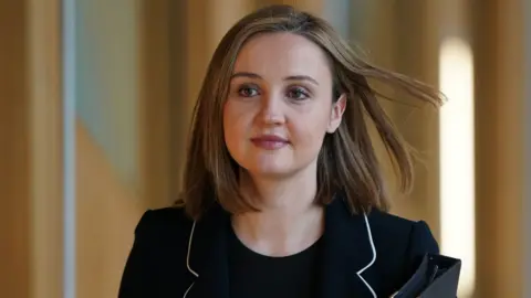 PA Media A woman with light brown hair, wearing a dark suit, in a medium close-up shot as she walks in the Scottish Parliament 