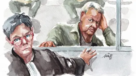 A court sketch of a man with short grey-white hair wearing a khaki shirt with a female lawyer with dark grey short hair and red-framed glasses in front of him