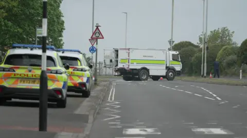 Police vehicles and a bomb disposal vehicle parked on an empty road. 