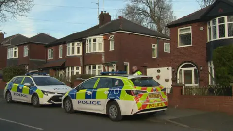 Two police cars parked on the kerb of a residential street outside a semi-detached house.