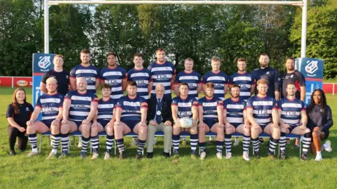 BRUFC The current Banbury men's team photo taken on the pitch by the posts - the team members are wearing navy and white striped T-shirts and socks and navy shorts