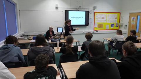 Students in class being spoken to by a teacher on consent