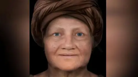 The early reconstruction of the face of The Kendal Woman. She is a middle-aged woman wearing a dark brown turban and she has blue eyes.