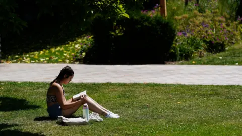 A woman sits on the grass reading a book.