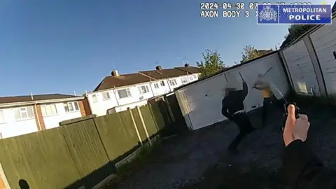 Metropolitan Police Screengrab of bodycam footage as an officer holds up a baton as he confronts a man with a long samurai-style sword who is wearing a yellow top. Another officer's arm can be seen spraying pepper spray