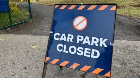 A blue and orange sign with Car Park Closed written on it in front of the entrance tot he car park at St George's Football Club.