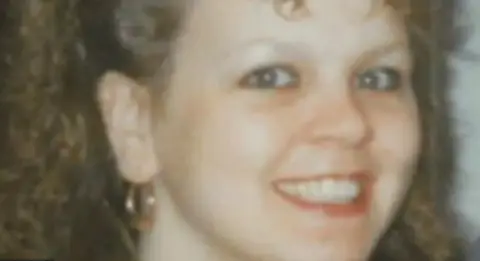 Suffolk Police Amanda Duncan smiling at the camera. She has brown curly hair and is wearing gold hoop earrings. 