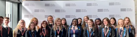 Yasmin Norvill A group of smiling school pupils, standing in front of banners and signs advertising the Edinburgh International Book Festival.