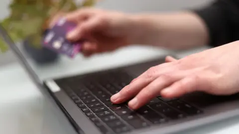 A person's hands using a laptop as they hold a bank card.