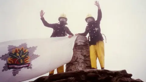 David Needham An old-style image of two fire fighters on the top of a mountain