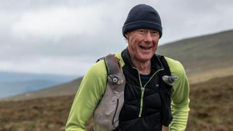 Tim Robinson smiling while running in the Highlands in his running attire and a woollen hat