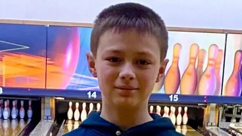 Leo looking straight at the camera. Ten-pin bowling is behind him with an alley leading to a set of pins.