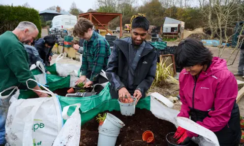 YoungMinds/Stewart Williams. Six gardeners with pots and earth in a garden centre