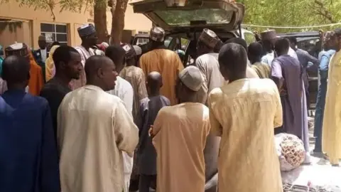 Traders and buyers stand as good are loaded into a car at the Jilli market along the Yobe-Borno state border in Nigeria