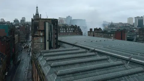 Getty Images An aerial view from the south west as firefighters continue to damp down the remains of a fire in a building at the north east corner of Glasgow Central Station. The Victorian grid streets are seen around the glass roof of the railway station. 