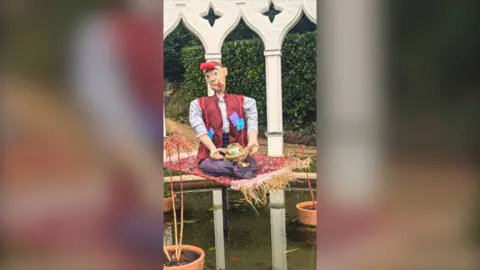 Painswick Rococo Garden A scarecrow on a floating carpet that has red hair and a red jacket.