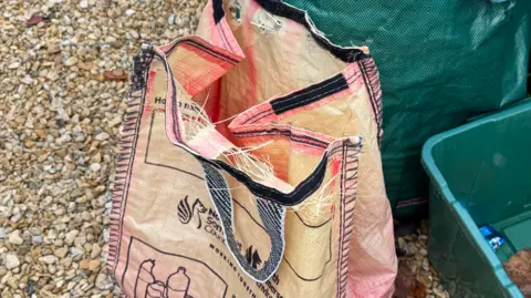 BBC Faded red North Somerset recycling bag, with holes along the top seam.