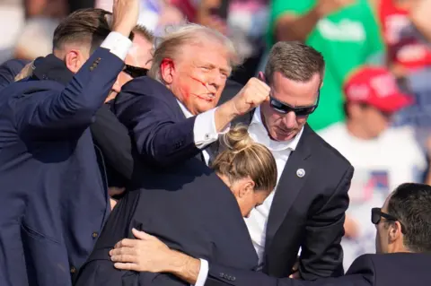 AP Republican presidential candidate former President Donald Trump is helped off the stage at a campaign event in Butler, Pa., on Saturday, July 13, 2024. 