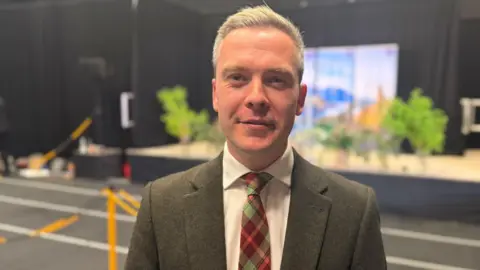 David Green has grey hair and is wearing a suit.