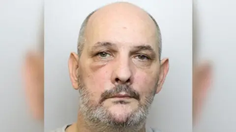 Avon and Somerset Police Mugshot of a man with a grey beard and balding grey hair. He is wearing a grey t-shirt.