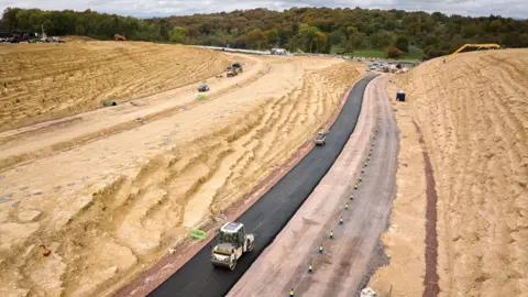 National Highways Aerial view of vehicles travelling along a concrete road with a large sand piles on either side.