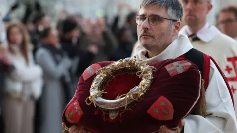 Getty Images A knight of the Order of the Holy Sepulchre holds the Crown of Thorns on a cushion during a procession to the Notre-Dame Cathedral. 