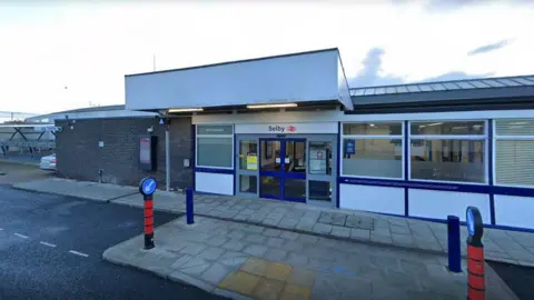 Google Exterior of Selby train station- a one storey brick building with a path outside.