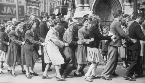 Getty Images People in 1945 join together in a conga line in Leicester in front of crowds.