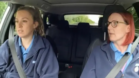 Two community children's nurses are in the front seat of a car, driving to their next destination. The photo is taken from a GoPro camera positioned on the dash of the car.