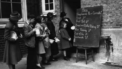 Harry Todd/Fox Photos/Getty Images 30th September 1940: People look at a basic menu while queuing to get into a makeshift canteen.