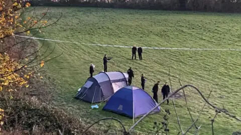 Two blue tents are surrounded by police in a field at the scene of the stabbing.