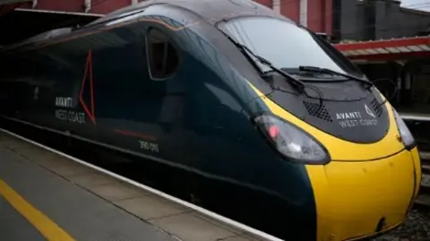 A dark green Avanti West Coast train stops at a train platform