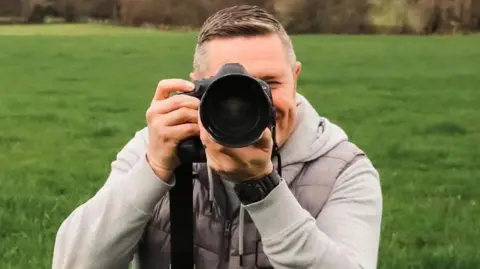 Jonathan Sterritt Pet Photography A man crouching in a grassy field looking down the lens of a camera.