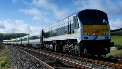 Enterprise train, silver with green and yellow paint details, travelling on tracks in countryside with blue sky and clouds 