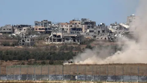 EPA-bestandsfoto waarop stof te zien is dat opstijgt van achter een Israëlische tank nabij het grenshek tussen Israël en Gaza, met het Shejaya-district van Gaza-stad op de achtergrond (29 juni 2024)