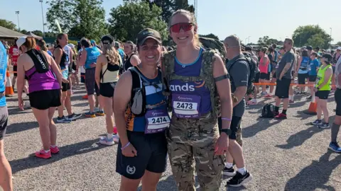 Lucy Kisielewska Two people stood next to each other smiling, one is in camo gear and has a large bag