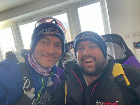 Alastair Crawford Two men smile at the camera wearing winter clothings.