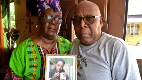 Margaret and Ronnie Charles sit by a window at their Moruga home holding a photo of Shakeem