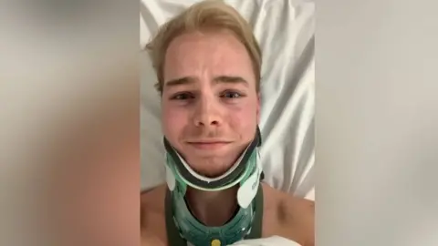PA Media A selfie of Ellis Pears in hospital wearing a green neck brace. He has short blond hair and his chest is covered with a white hospital sheet.